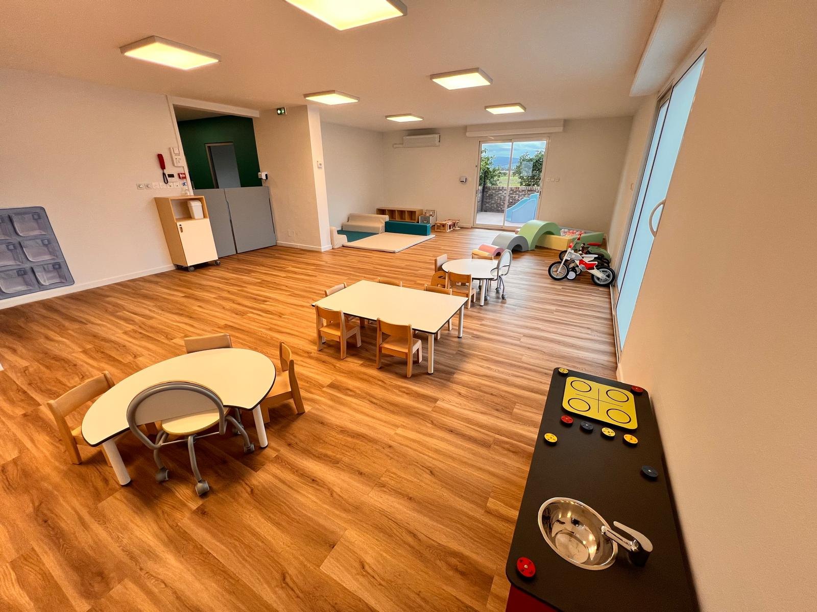 Grande salle de vie de la micro-crèche Mélisse à Dachstein, avec tables et chaises à hauteur d’enfant et accès direct à la terrasse